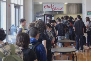 A group of students lined up in the BHS cafeteria for lunch. A banner overhead displays "Chef