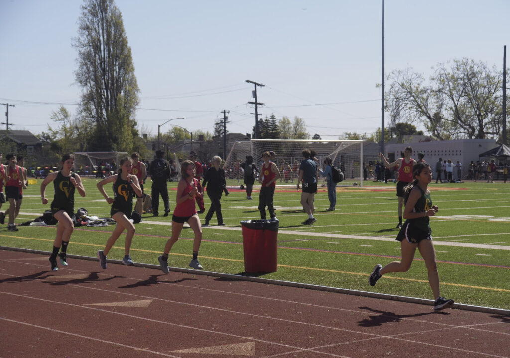 There are several people in sports uniforms running on a track.