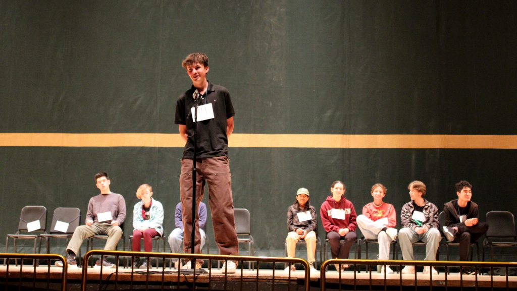 Calder Corson speaks into the microphone on stage at the first annual Spelling Bee.